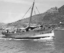 Vaixell de vela llatina prop de la costa de Roses. En darrer terme es pot veure el far i les ruïnes del castell de la Trinitat. 1930-1940